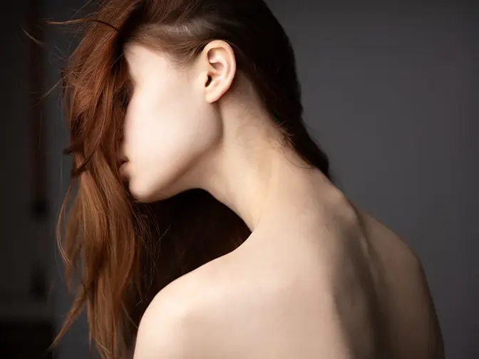 A woman with beautiful healthy hair falling over her face showing the slender and pale back of her neck